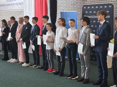 Uczniowie i nauczyciele odbierający nagrody i stojący na tle polskiej flagi