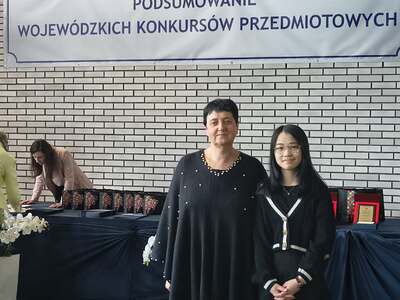 Uczniowie i nauczyciele odbierający nagrody i stojący na tle polskiej flagi